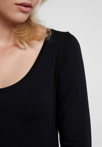 Musta pitkähihainen paita, jossa on pyöreä pääntie, valmistettu silkkisestä kankaasta. Ominaisuuksiin kuuluu sovitettu siluetti ja minimaalinen ompelu.