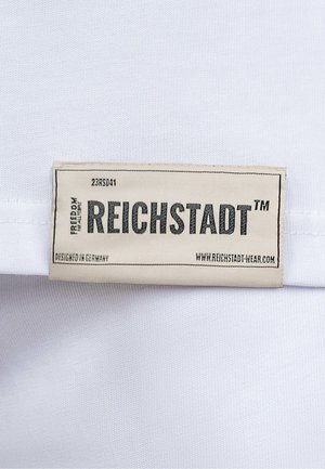 Tessuto bianco con una superficie liscia presenta un'etichetta orizzontale in un tenue beige, con la scritta "REICHSTADT™" e informazioni sulla cura.