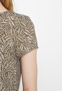 Chemise vert olive à manches courtes avec un motif de feuilles blanches, fabriquée dans un tissu doux. Le design comprend une encolure arrondie.