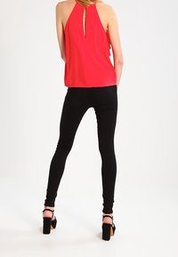 Top rojo sin mangas con detalle de escote en la espalda, combinado con jeans ajustados negros y sandalias de tacón alto negras. Tejido suave y diseño ajustado.