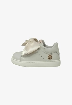 Sneaker bianco low-top con grandi lacci a fiocco in raso e un piccolo charm metallico rotondo con logo sul lato.