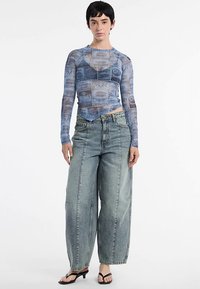 Long-sleeve, sheer blue top with a printed design; paired with loose, light-wash denim jeans and black heeled sandals.