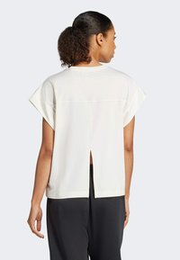 Witte top met korte mouwen, een split aan de achterkant en een ronde hals, gemaakt van zachte stof. Gecombineerd met donkere, losse broek.
