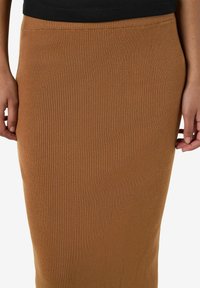 Jupe midi ajustée à rayures verticales en marron chaud, en tissu extensible. La ceinture est lisse et plate.