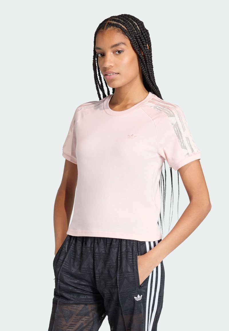 T-shirt sportif à manches courtes de couleur rose clair avec un col rond, présentant des accents en maille texturée sur les épaules et un marquage minimaliste.