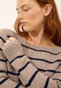 Beżowy sweter dziany w niebieskie paski, z szerokim dekoltem i ściągaczami. Miękka tekstura, luźny krój, skupiony na swobodnym komforcie.