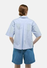 Chemise à manches courtes bleu clair avec un design à dos plissé, dotée d'un col classique et d'une coupe décontractée, portée avec un short en denim.
