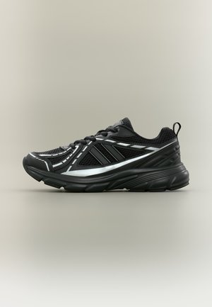 Sneaker atletica nera con tomaia in mesh e sintetico, dettagli riflettenti argento, chiusura con lacci e suola spessa e imbottita, vista laterale.