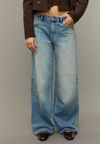 Lichtblauwe wijde jeans van denim, met een hoge taille, vervaagde was en een rafelige zoom. Gecombineerd met donkere schoenen en een bruin kort jasje.