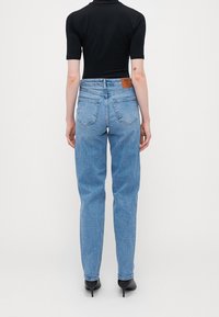 Světle modré džíny s vysokým pasem a rovnou nohavicí, které mají dvě zadní kapsy. Na pásku je hnědá kožená etiketa. Hladký denimový povrch.