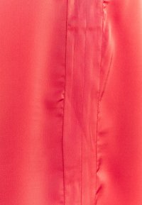 Gros plan sur un tissu rouge lisse avec une couture verticale et de légères rides le long de la ligne de couture.