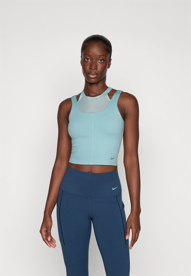 Un crop top de sport bleu clair avec un détail en maille et des bretelles larges, associé à un legging taille haute bleu foncé, les deux portant les logos Nike.