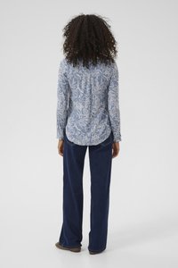 Langärmliges blaues Hemd mit weißem Blumenmuster, geknöpftem Kragen und abgerundetem Saum. Kombiniert mit lockeren, dunkelblauen Jeans.