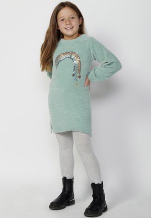 Vestido de punto verde menta con un diseño de lentejuelas arcoíris. Combinado con leggings grises y botas negras de tobillo. Mangas largas y aberturas laterales.