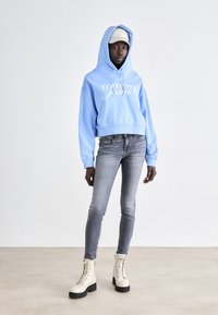 Ljusblå cropped hoodie med vit "tommy jeans" logotyp, parat med grå jeans och beige snörkängor med svarta sulor.