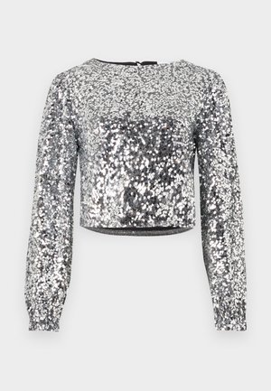 Silberner, glitzernder Cropped-Top mit langen Ärmeln, runder Ausschnitt und rückseitigem Reißverschluss. Glatte Textur mit einem glänzenden, reflektierenden Finish.