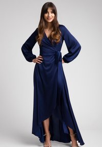 Granatowa sukienka kopertowa z długimi rękawami, dekoltem w kształcie litery V i wysokim rozcięciem. Wykonana z gładkiego materiału, z wiązanym detalem w pasie i płynącym krojem hemu.