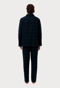 Σετ πιτζάμας καρο σε σκούρο πράσινο και ναυτικό μπλε, κατασκευασμένο από μαλακό ύφασμα. Διαθέτει πουκάμισο με κουμπιά και γιακά, καθώς και παντελόνια σε χαλαρή εφαρμογή.