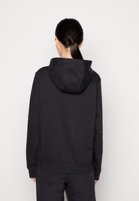 Svart huvtröja med avslappnad passform, med en känguruficka och ribbade muddar. Slät textur, minimalistisk design.