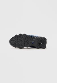 Black sneaker sole with textured grip pattern, featuring a blue and black upper design. Includes a round accent near the heel.