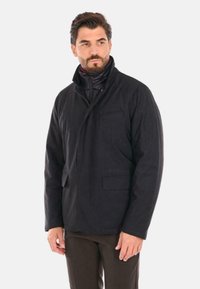 La giacca nera presenta un colletto alto, zip frontale e due tasche laterali. Realizzata in tessuto morbido con una finitura liscia e una vestibilità su misura.