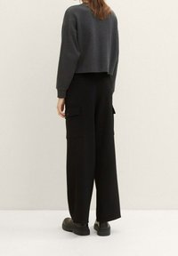 Pantalones cargo anchos negros con bolsillos laterales y cintura alta, combinados con un sudadera gris corta de un tejido suave y texturizado.
