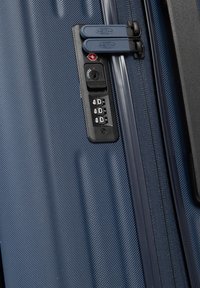 Valigia rigida blu navy con superficie testurizzata, doppia zip, lucchetto a combinazione e maniglia robusta sul lato.