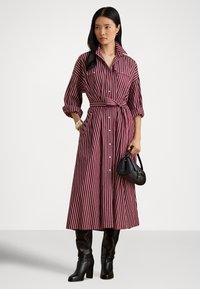 Stripete skjortekjole i burgunder og hvitt, med krage, knapper foran, belte med knyting og lange ermer. Kombinert med knelange svarte støvler og en håndveske.