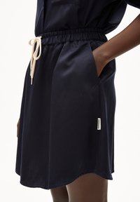Marineblauwe jurk met een elastische tailleband, trekkoorddetails en zijzakken. Soepele textuur, licht gebogen zoom, met een merketiket.