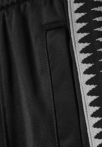 Schwarzer Stoff mit einem strukturierten Design und einem grauen Zickzack-Muster. Enthält eine Seitentasche, die in die Naht integriert ist.