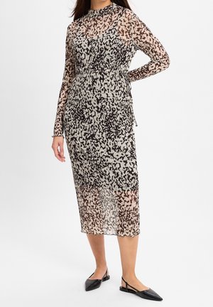 Frau trägt ein langärmliges, schwarz-beiges, gepunktetes Midikleid mit tailliertem Bund und schwarzen spitzen Slingback-Ballerinas.