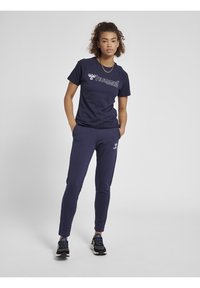 Mørkeblå sportstøj sæt bestående af en t-shirt med hvid logo og matchende tætsiddende bukser. Stoffet ser blødt ud; bukserne har en subtil tekstur.