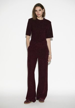 Bordeauxrode jumpsuit van glanzende stof met korte mouwen, wijde pijpen en een getailleerd ontwerp. Soepele textuur, minimalistische stijl.