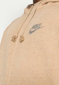 Beige hoodie made from textured fabric with specks of color. Features a drawstring hood and a multicolored Nike logo on the chest.