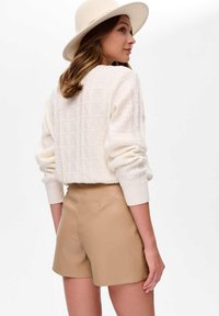 Kremowy sweter dzianinowy z geometrycznym wzorem, w połączeniu z beżowymi szortami z syntetycznej skóry, o luźnym kroju i ściągaczach na rękawach oraz w pasie.