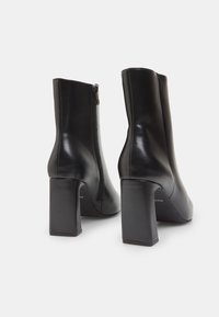 Black leather ankle boots with a smooth texture, square heels, and a side zip closure. Features a fitted design and minimal detailing.
