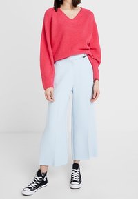 Un pull rose à col en V associé à un pantalon large bleu clair et des baskets montantes noires. Le pull a une coupe décontractée et une texture côtelée.