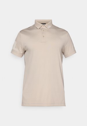 Bež majica polo izrađena od glatkog materijala, s ovratnikom, dugmetom na tri gumba i suptilnim uzorkom na lijevoj rukavu.