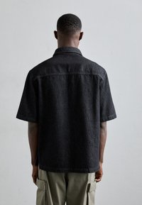 Camicia in denim nera a maniche corte con colletto classico e tessuto testurizzato, caratterizzata da una vestibilità dritta e fessure laterali per il comfort.