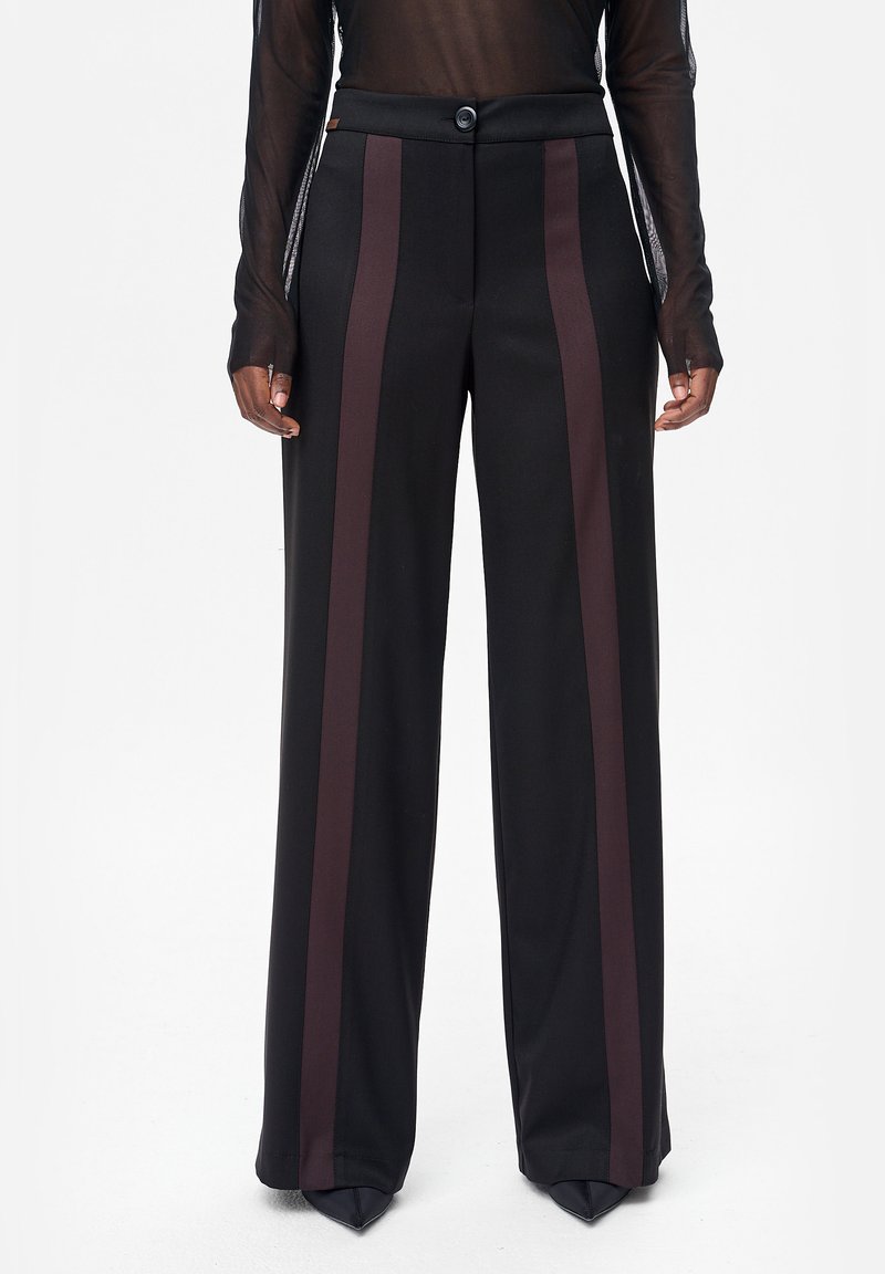 Czarne szerokie spodnie z ciemnobrązowymi pionowymi paskami, noszone z czarnymi szpiczastymi butami i przezroczystą bluzką z długim rękawem.