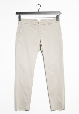 Beige bukser med lige ben, bærestropper, sidelommer og knaplukning, hængende på en sort bøjle mod en hvid baggrund.