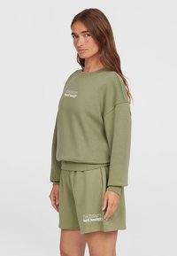 Completo felpa e pantaloni corti verde oliva realizzato in morbido materiale, con scollatura a coste e logo stampato sui pantaloni.