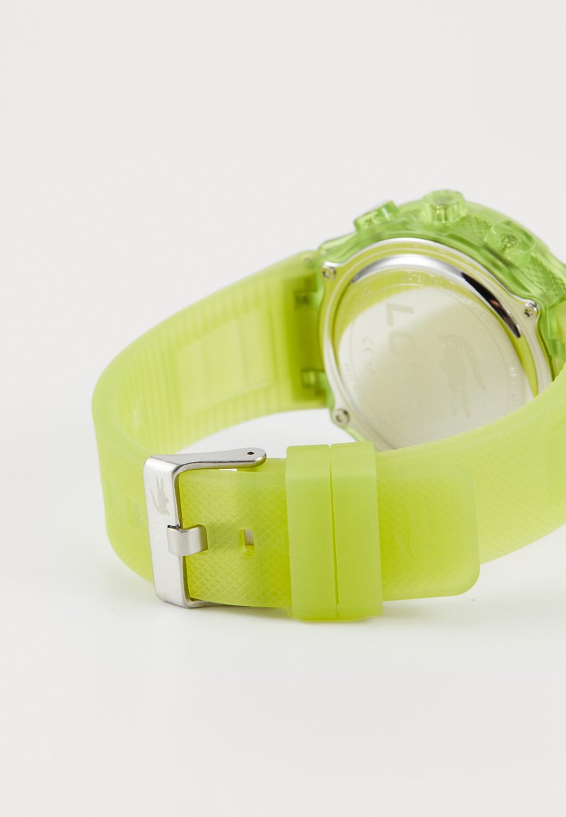 Reloj de silicona verde lima con correa texturizada, hebilla de acero inoxidable y caja transparente. La parte posterior no muestra marcas visibles.