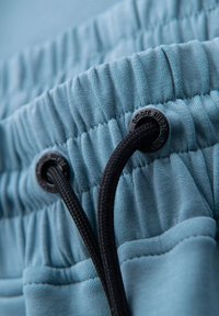 Jasnoniebieski materiał o strukturalnej powierzchni, z czarnym sznurkiem i oczkami. Design obejmuje marszczone szwy dla swobodnego dopasowania.