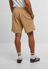 Beige bomullshorts med elastisk midje, baklomme og avslappet passform, kombinert med stripete sokker og casual sko.