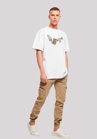 White cotton t-shirt with colorful cartoon character print on the front, paired with beige cargo pants and white sneakers.
