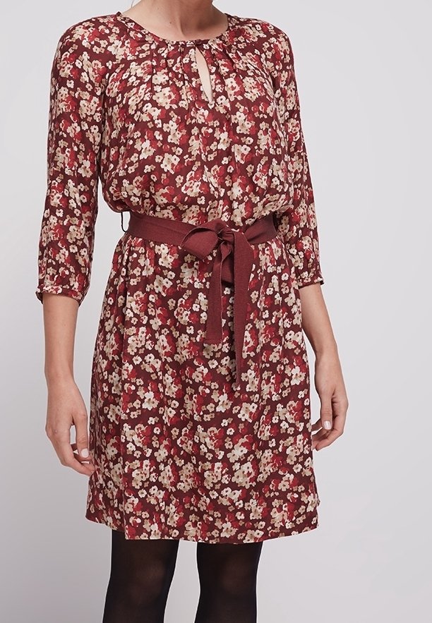 Femme portant une robe florale bordeaux mi-longue avec des manches trois-quarts et une ceinture assortie en tissu nouée à la taille.