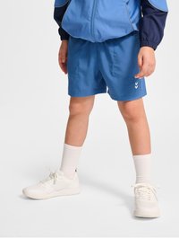 Blå sportshorts i lätt tyg med sidofickor, kombinerat med vita sneakers och strukturerade vita strumpor.