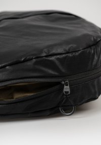 Borsa circolare nera realizzata in tessuto liscio e resistente, con zip superiore, un pratico tirazip metallico e una foderatura interna a contrasto marrone.