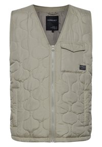 Padded vest in light beige with quilted pattern, front zipper, and a small chest pocket. Made of smooth polyester material.